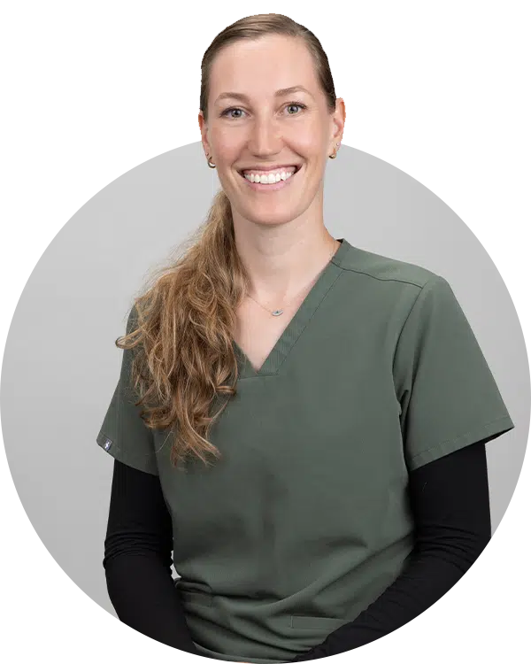 A smiling woman in green scrubs with a long, wavy hairstyle is seated in front of a neutral background. The image showcases her friendly expression, representing the Joybound Team on the 'Meet the Team' page.