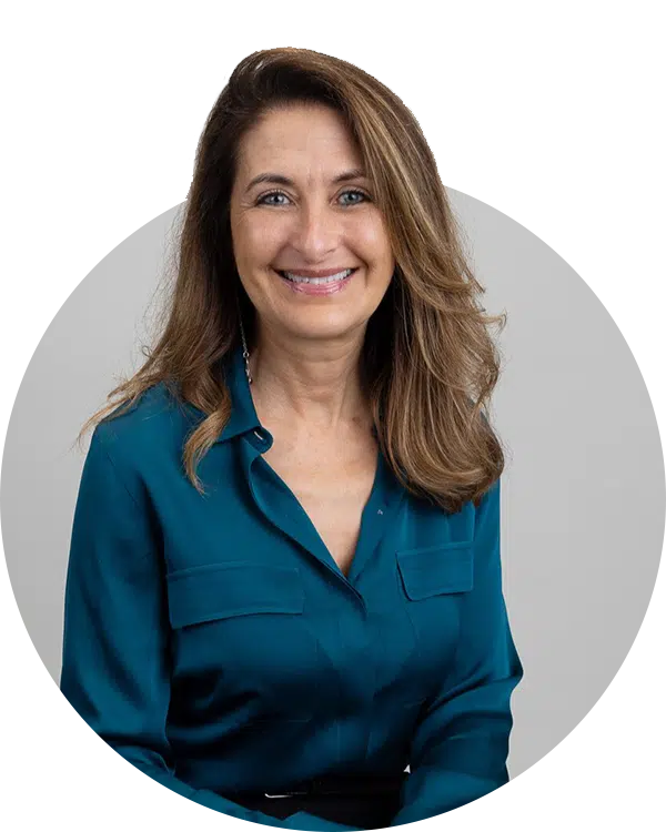 A smiling woman with long, wavy brown hair wearing a teal blouse is photographed against a neutral background. This image is part of the Joybound Team section, highlighting team members.
