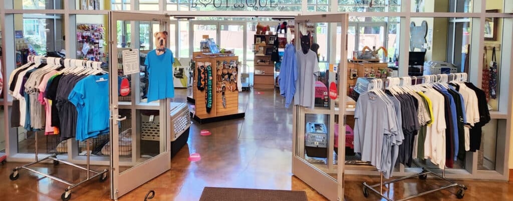 Inside a retail store featuring display racks with various colored shirts, including blue, pink, and white. The entrance is framed by glass doors, and additional merchandise is visible in the background, with a focus on an organized shopping space. Related to Joybound.