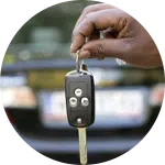 A hand holding a car key in front of a vehicle. The key has buttons for locking and unlocking the car, while the blurred background shows the rear of a parked car. This image relates to animal rescue donations through vehicle contributions.
