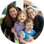 Two adults and two children smiling together, each with colorful face paint resembling animal features. The group is standing outdoors, showcasing a friendly atmosphere, highlighting community engagement and programs promoting rescuing animals in need.