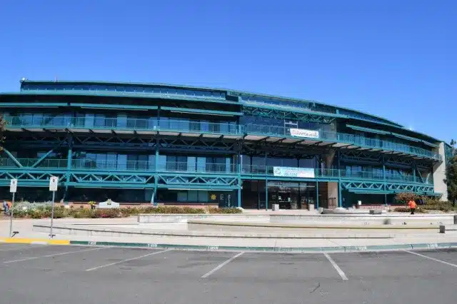 A modern building with a blue-green exterior and large glass windows, featuring a sign for a veterinary service. The structure has multiple levels and is surrounded by a parking lot and landscaped areas.