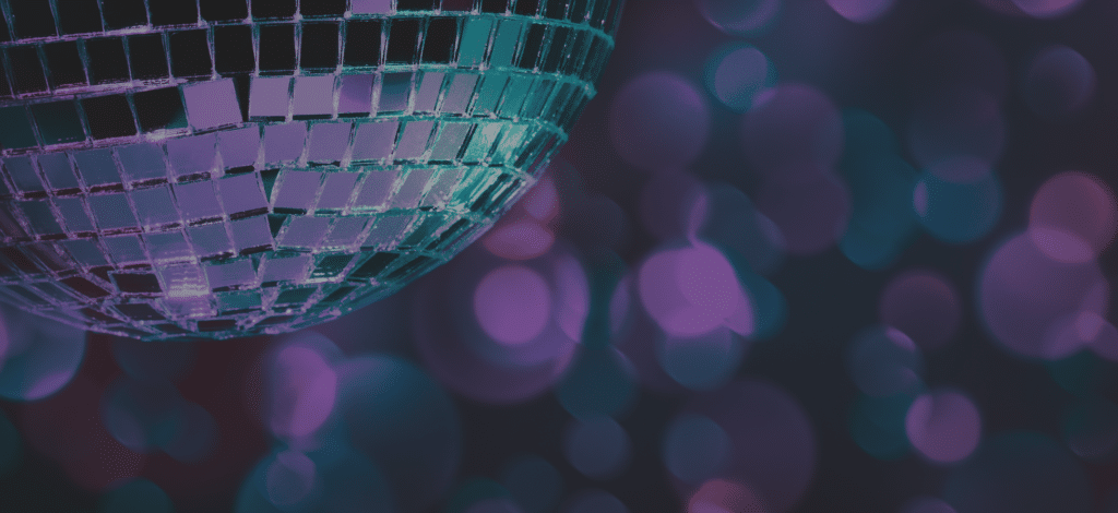 A close-up of a disco ball reflecting light against a blurred purple and teal bokeh background. The disco ball features multiple mirrored squares, casting shimmering highlights across the scene.