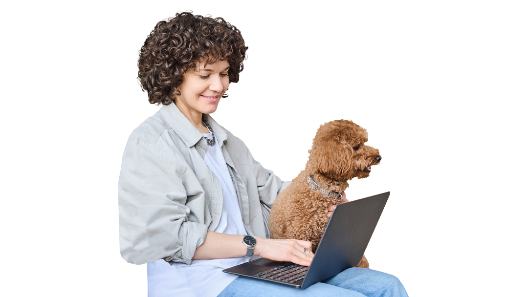 A woman with curly hair wearing a gray jacket sits with a laptop on her lap. A small dog sits next to her, looking toward the screen. The background is plain, focusing on the woman and the dog, highlighting their interaction.