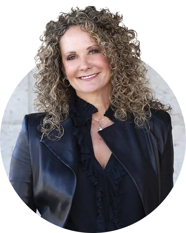 A woman with curly hair in a dark blazer and ruffled blouse, posed against a light gray background for the Joybound Board of Directors.