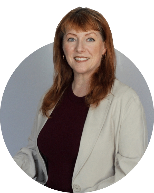 A woman with auburn hair in a beige blazer and burgundy top, shown in a circular portrait against a gray background for Joybound donate items.