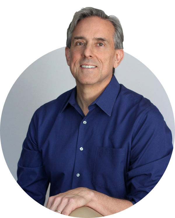 A gray-haired man in a blue button-down shirt poses for a portrait against a light gray circular background for Joybound donate items.