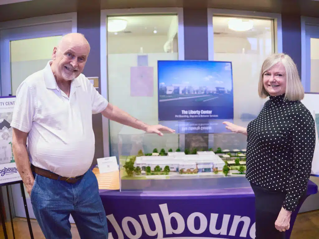 A man and woman stand beside a tabletop model of The Liberty Center displayed in a glass case at a groundbreaking ceremony.
