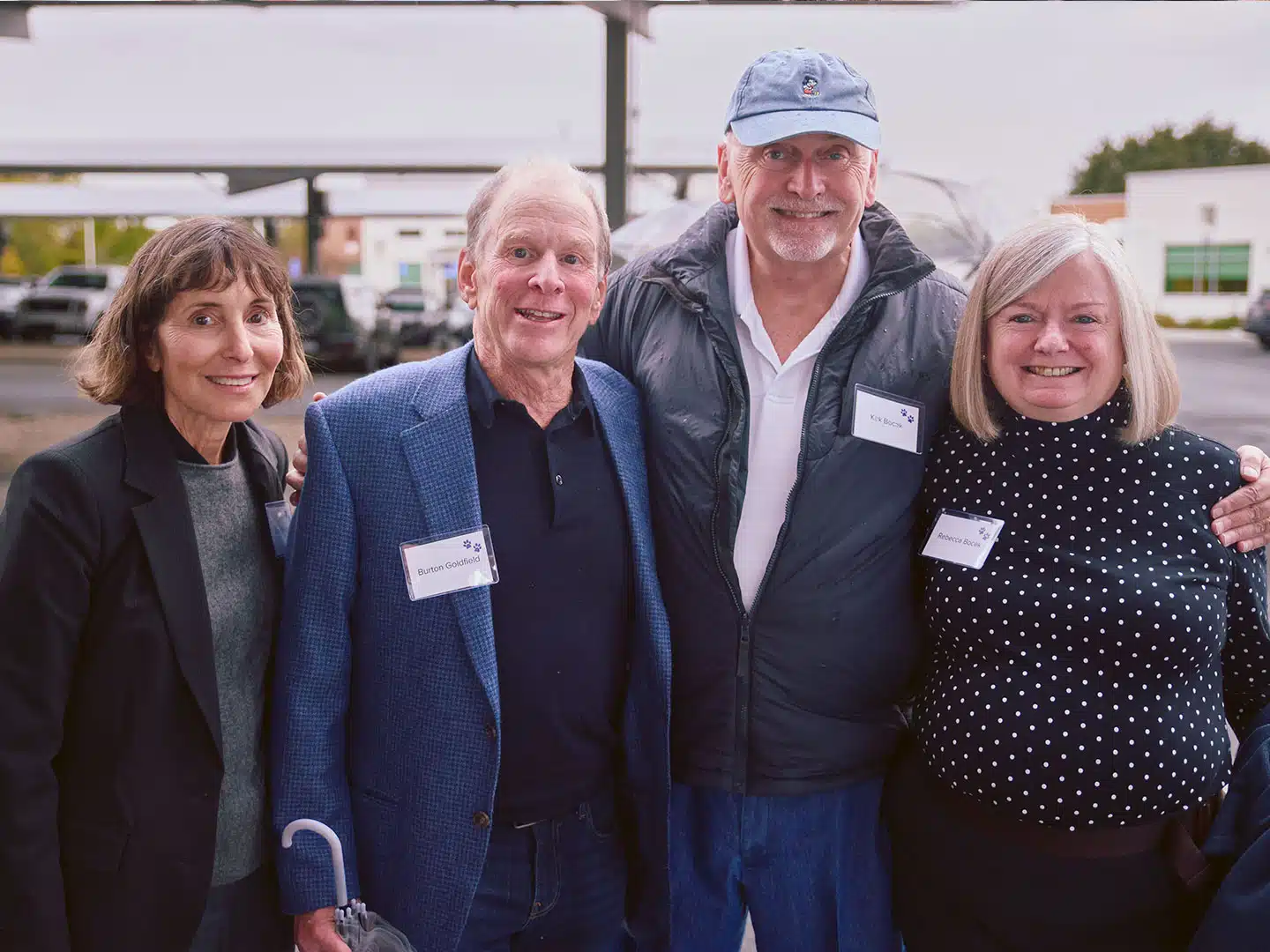 Four adults stand together outdoors at the Liberty Center groundbreaking ceremony, with parking lot buildings visible in the background.