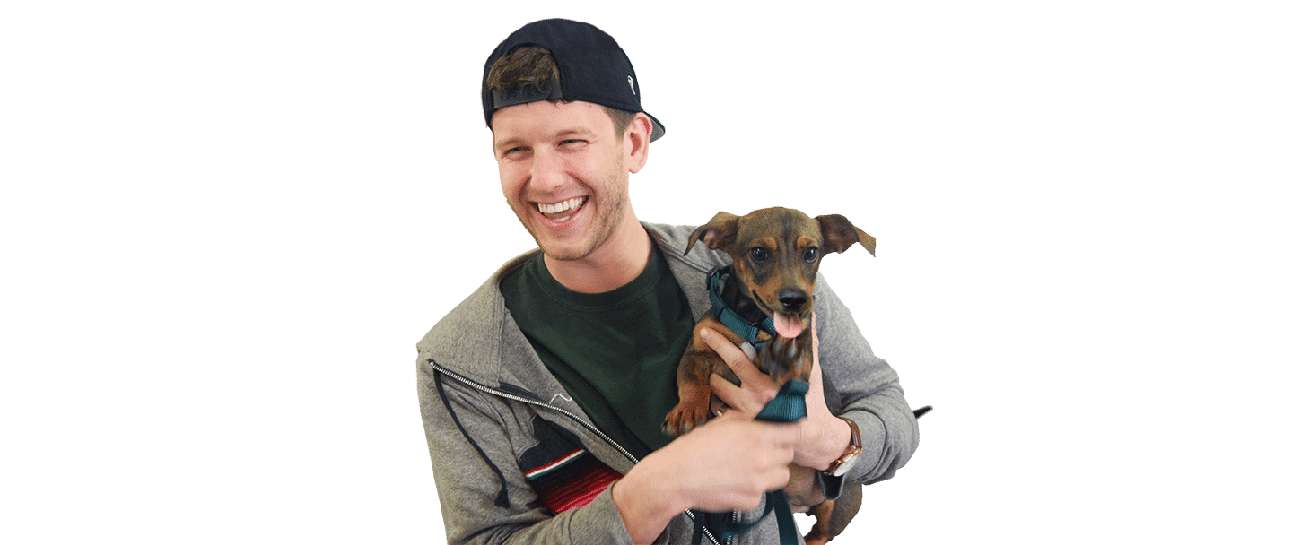 A smiling man in a cap holds a small brown dog, isolated on a transparent background, for Joybound.