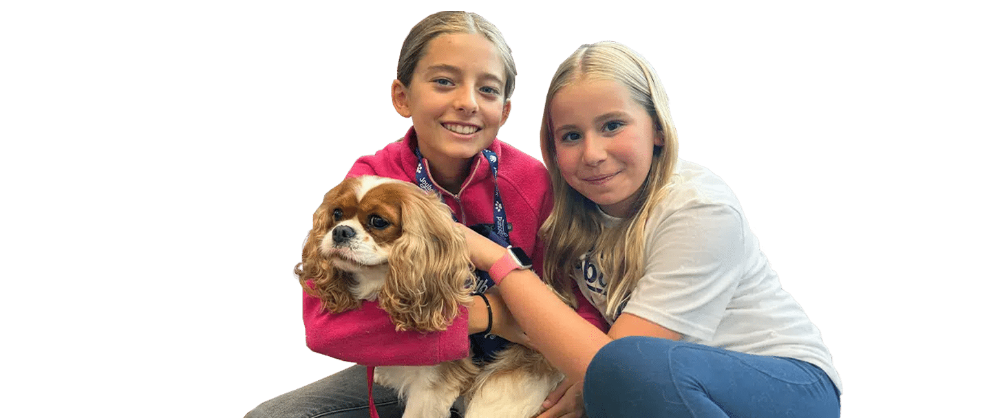 Two girls sit together holding a small dog, with Joybound in a cutout-style image on a plain background.