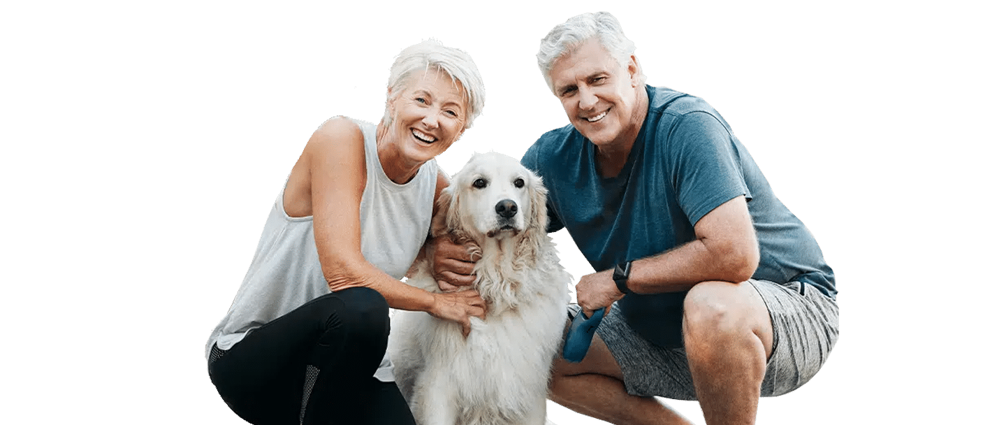 A smiling older couple crouches beside a white dog, with Joybound appearing as the likely shelter or organization context.