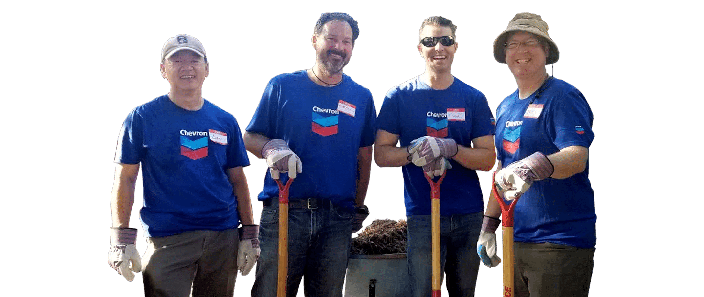 Four Joybound staff members in blue shirts and gloves stand outdoors beside shovels and a wheelbarrow.