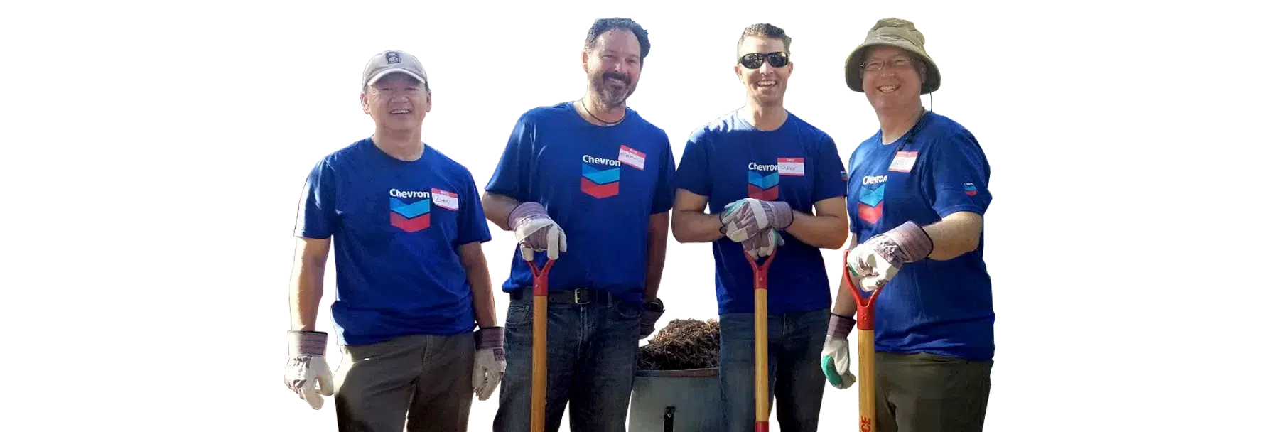 Four Joybound staff members in blue shirts and gloves stand outdoors beside shovels and a wheelbarrow.