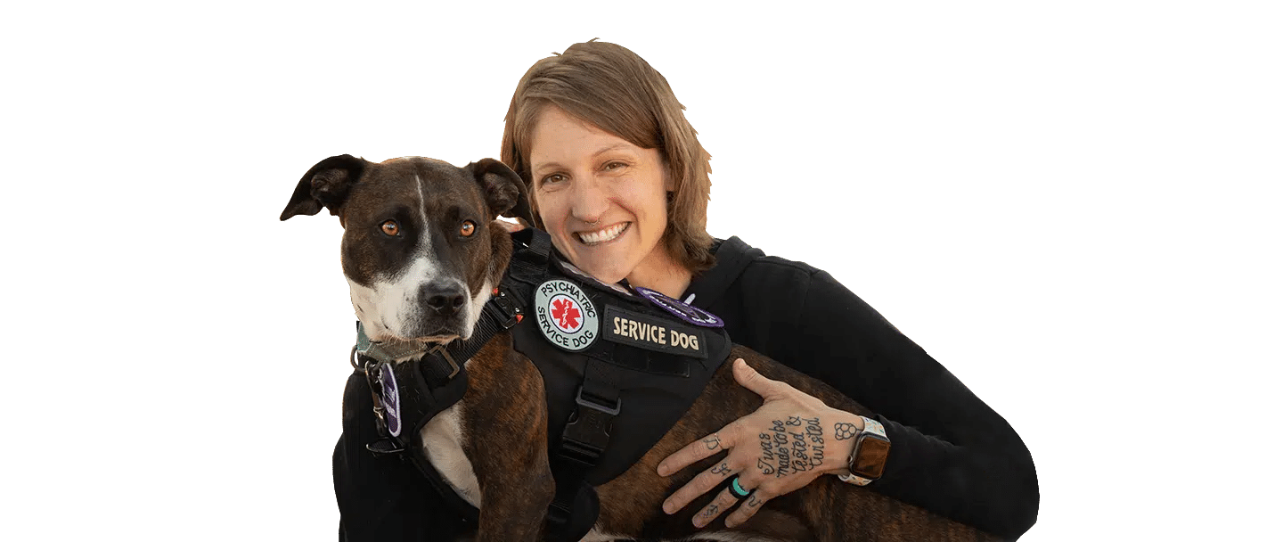 A woman embraces a brown-and-black Psychiatric Service Dog wearing a service vest against a black background.