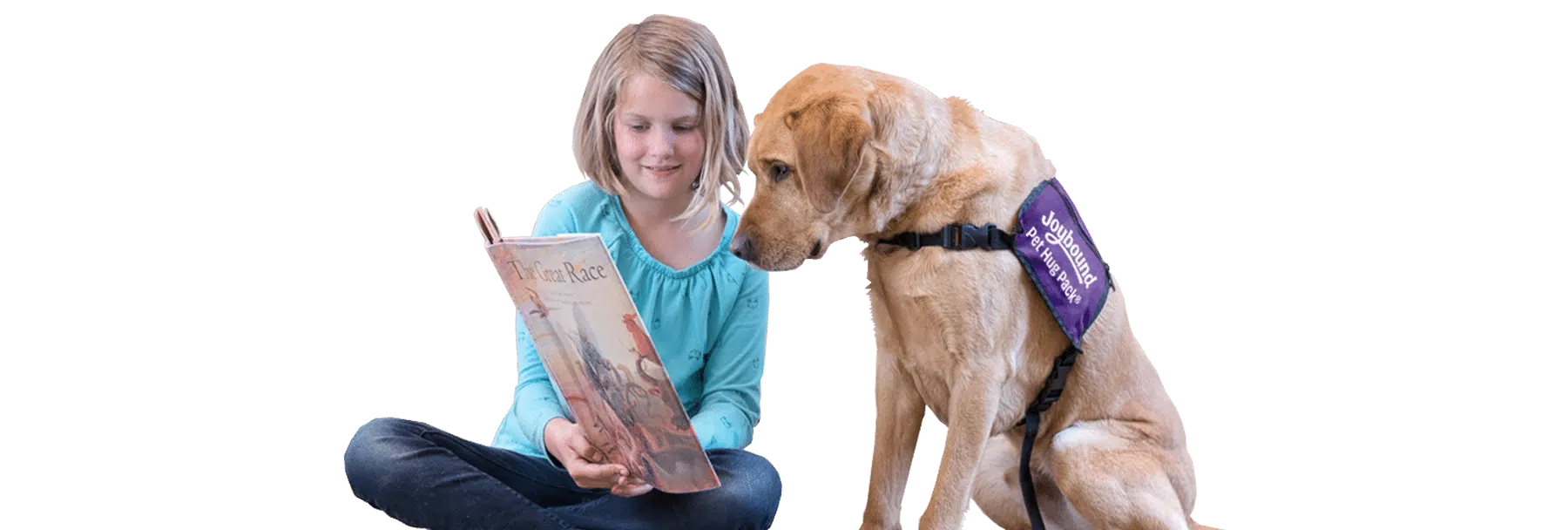 A young girl sits beside a yellow Labrador wearing a purple Joybound vest while holding an open book, against a white background.