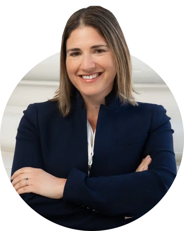 A woman in a navy blazer with her arms crossed, posed in front of a light-colored background.