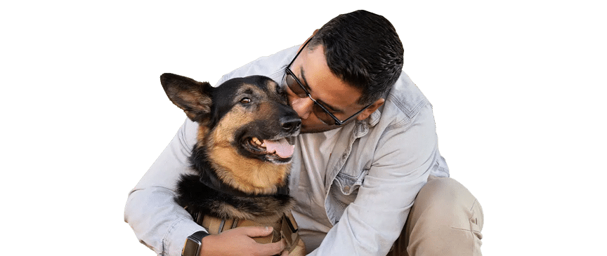 A man kneels and hugs a Service Dog, a German shepherd wearing a tan harness, against a white background.