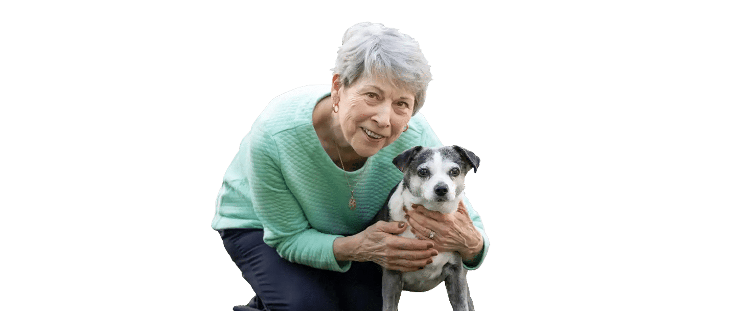 An older woman in a green sweater holds a small black-and-white dog, with Joybound included in the image context.