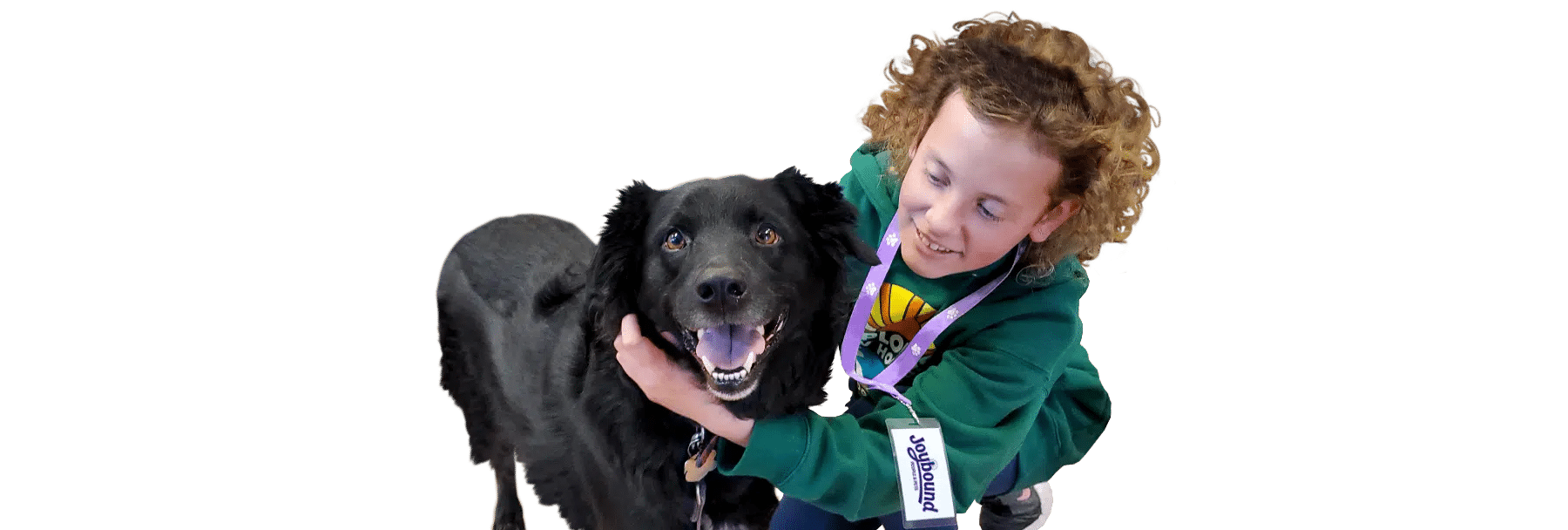 A curly-haired child in a green Joybound jacket hugs a black dog, isolated on a white background.